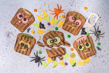 Funny halloween monster sandwiches. Set of various decorated monster sandwich and toasts, with cucumber, cheese and meat sausages, white table background with Halloween decorations