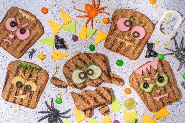 Funny halloween monster sandwiches. Set of various decorated monster sandwich and toasts, with cucumber, cheese and meat sausages, white table background with Halloween decorations