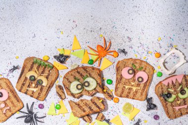 Funny halloween monster sandwiches. Set of various decorated monster sandwich and toasts, with cucumber, cheese and meat sausages, white table background with Halloween decorations