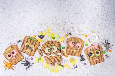 Funny halloween monster sandwiches. Set of various decorated monster sandwich and toasts, with cucumber, cheese and meat sausages, white table background with Halloween decorations