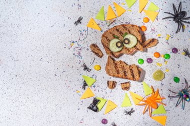 Funny halloween monster sandwiches. Set of various decorated monster sandwich and toasts, with cucumber, cheese and meat sausages, white table background with Halloween decorations