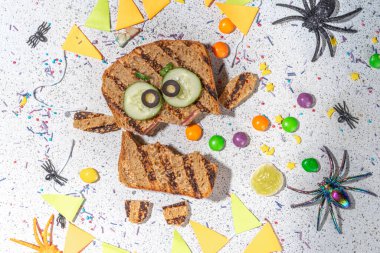 Funny halloween monster sandwiches. Set of various decorated monster sandwich and toasts, with cucumber, cheese and meat sausages, white table background with Halloween decorations