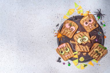 Funny halloween monster sandwiches. Set of various decorated monster sandwich and toasts, with cucumber, cheese and meat sausages, white table background with Halloween decorations