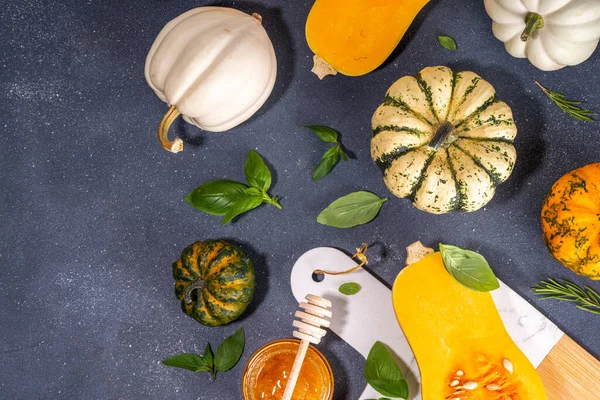Pumpkins cooking background with various sizes, types and colors squashes with  herbs and spices, olive oil, honey, on black kitchen table background Top view copy space