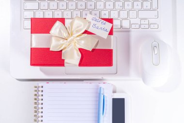 İş yerindeki gizli Noel Baba 'dan hediye. Ofis Noel ve Yeni Yıl kutlama oyunu. Ofis masası yüzeyi, neşeli hediye kutusu olan defter, beyaz arkaplan düz kopya alanı