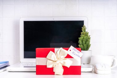 İş yerindeki gizli Noel Baba 'dan hediye. Ofis Noel ve Yeni Yıl kutlama oyunu. Ofis masası yüzeyi, neşeli hediye kutusu olan defter, beyaz arkaplan düz kopya alanı