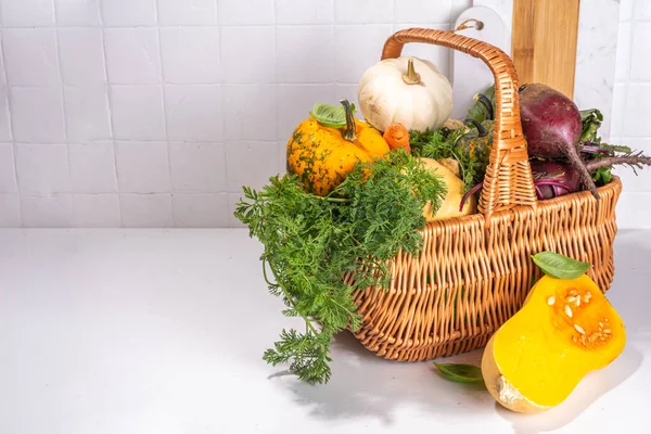Autumn cooking, organic farm food background. Harvesting concept. Basket with fresh vegetables colorful pumpkins, squash, beetroot, carrots, cabbage, on a white marble table. cooking background