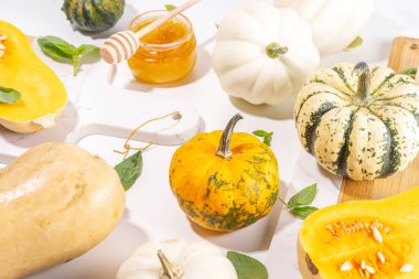 Bal kabakları değişik boyutlarda, çeşitli boyut ve renklerde kabaklar, bitki ve baharatlar, zeytin yağı, bal, beyaz mutfak masası arka planında üst görünümde fotokopi alanı 