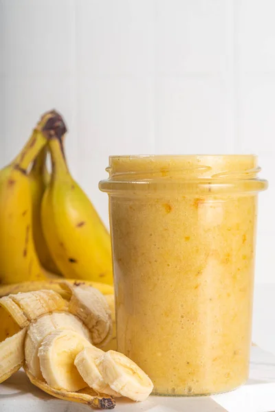 Bananas jam in small glass jar with fresh bananas on  white table background