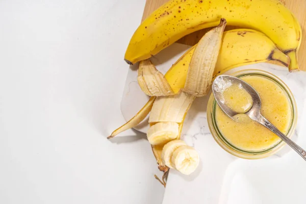 Bananas jam in small glass jar with fresh bananas on  white table background