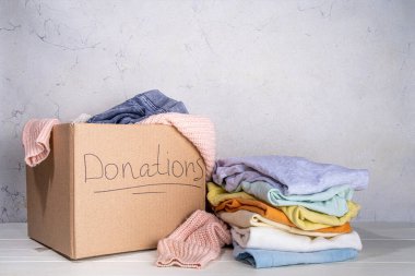 Giysileri, oyuncakları ve yiyeceği beyaz masa arkasında olan bağış kutusu. Oyuncak, kadın ve çocuk kıyafetleri ve yiyeceklerle dolu bir karton bağış kutusu. Sosyal hizmet, gönüllülük, yardım konsepti kopyalama alanı