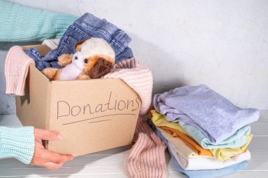 Giysileri, oyuncakları ve yiyeceği beyaz masa arkasında olan bağış kutusu. Oyuncak, kadın ve çocuk kıyafetleri ve yiyeceklerle dolu bir karton bağış kutusu. Sosyal hizmet, gönüllülük, yardım konsepti kopyalama alanı