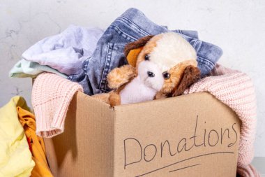 Giysileri, oyuncakları ve yiyeceği beyaz masa arkasında olan bağış kutusu. Oyuncak, kadın ve çocuk kıyafetleri ve yiyeceklerle dolu bir karton bağış kutusu. Sosyal hizmet, gönüllülük, yardım konsepti kopyalama alanı