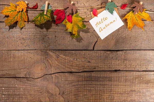Creative autumn frame border composition with fall leaves. Red and yellow autumn leaves hang on clothesline rope, on wooden background copy space for text