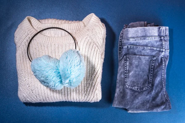 Set of female winter autumn clothes. Jeans, white knitted sweater and hat,  mittens and sneakers on  dark blue background. Casual cozy fashion outfit flat lay