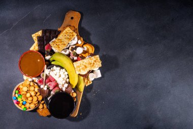 S 'mores ev yemeği ve malzemeler. Marshmallow, kraker, çikolata, meyve, çikolata, sos içeren açık büfe tabağı. Geleneksel sonbahar Amerikan çörekleri tatlısı 