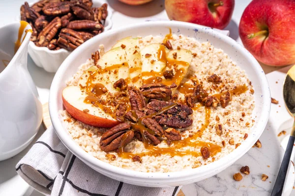 Simple autumn traditional American breakfast. Ready to eat apple pie oatmeal porridge with apples, pecans and caramel on white table background copy space