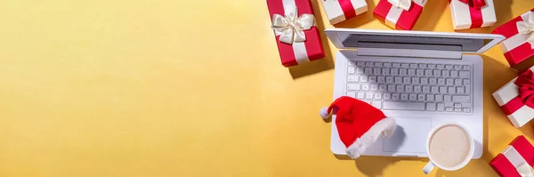 Christmas sale, preparation for holidays concept. Santa Claus hands with laptop, hot chocolate latte cup, gift boxes, flat lay on golden background. Making wishlist, preparation gifts for Christmas.