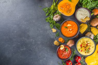 Farklı sonbahar çorbaları seti. Portakal kaselerinde çeşitli sebze çorbaları - mısır, patates, balkabağı, domates, kabak, brokoli kremalı çorba. Siyah beton arkaplanda üst görünüm kopyalama alanı