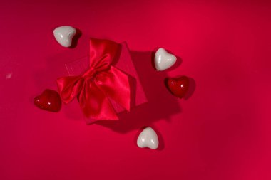 Sevgililer Günü tatili geçmişi. Kurdeleli el işi kağıt hediye kutusu, gül çiçekleri ve kalpler dekorasyonu, kırmızı arkaplan üst görünümü üzerinde kopyalama alanı