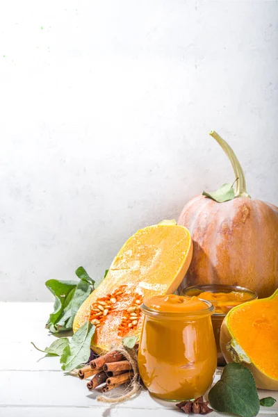 Sweet pumpkin pie jam. Homemade confiture with pumpkin puree and traditional autumn spices. cinnamon, anise. With fresh butternut squash and fall leaves on white wooden background
