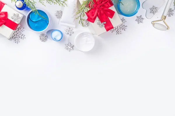 Winter skin care and hand care cosmetic in unbranded containers, bottles, tubes with artificial snowflakes, Christmas tree branches and gift boxes. Christmas New Year winter cosmetics sale flat lay