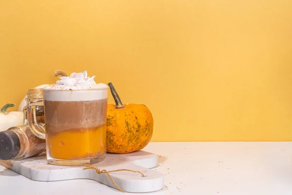 Glass cup with tasty pumpkin spice latte, with white and orange pumpkin squash, pumpkin pie spices and autumn decor copy space. Traditiional autumn Thanksgiving holiday drink