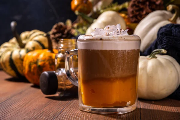 Glass cup with tasty pumpkin spice latte, with white and orange pumpkin squash, pumpkin pie spices and autumn decor copy space. Traditiional autumn Thanksgiving holiday drink