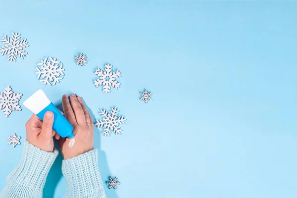 Woman using winter cream for hands. Girl hands with cream flat lay on light blue background with artifical snowflakes and different hand creams. Winter hand skin care cosmetics background