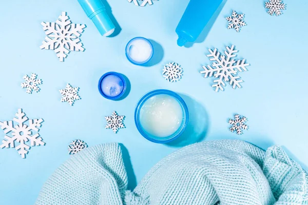 Winter skin care and hand care cosmetic in unbranded containers, bottles, tubes with artificial snowflakes on light blue background. Winter hand skin care cosmetics background top view copy space