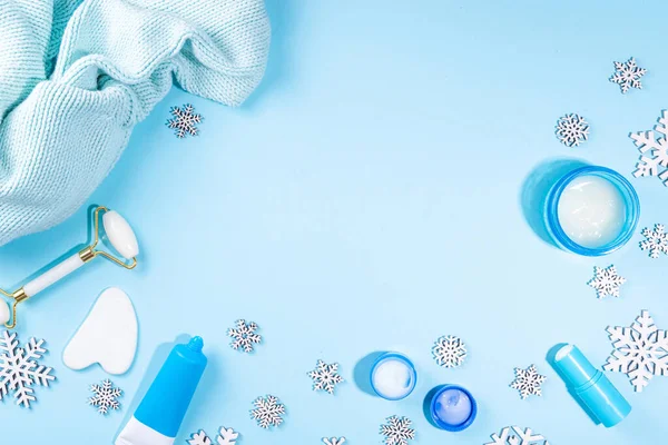 Winter skin care and hand care cosmetic in unbranded containers, bottles, tubes with artificial snowflakes on light blue background. Winter hand skin care cosmetics background top view copy space