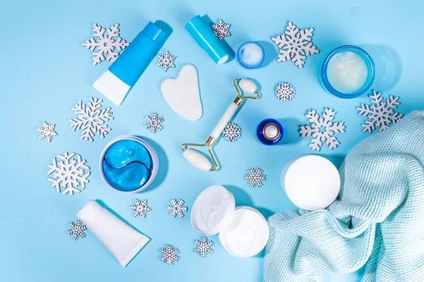 Winter skin care and hand care cosmetic in unbranded containers, bottles, tubes with artificial snowflakes on light blue background. Winter hand skin care cosmetics background top view copy space