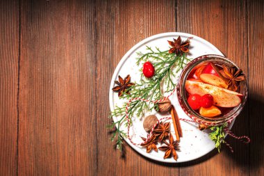 Tarçınlı sıcak şarap ve yıldız anason. Kış mevsimi meyvesi ve böğürtlen likörü, portakal, elma, kızılcık, baharat, Noel ağacı dalları ve ahşap masa üzerinde hediye kutuları olan sıcak meyve suyu. 