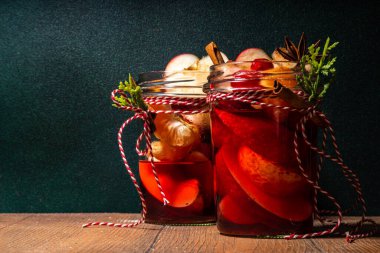 Tarçınlı sıcak şarap ve yıldız anason. Kış mevsimi meyvesi ve böğürtlen likörü, portakal, elma, kızılcık, baharat, Noel ağacı dalları ve ahşap masa üzerinde hediye kutuları olan sıcak meyve suyu. 