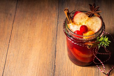 Tarçınlı sıcak şarap ve yıldız anason. Kış mevsimi meyvesi ve böğürtlen likörü, portakal, elma, kızılcık, baharat, Noel ağacı dalları ve ahşap masa üzerinde hediye kutuları olan sıcak meyve suyu. 