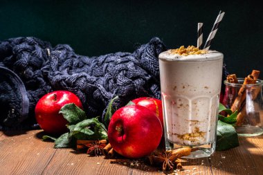 Ev yapımı elmalı turta milkshake, tart parçacıkları ve baharatlı kırmızı sonbahar elma proteini smoothie, sıcacık ahşap arka planda mevsimlik sağlıklı bir kahvaltı içeceği.