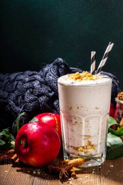 Ev yapımı elmalı turta milkshake, tart parçacıkları ve baharatlı kırmızı sonbahar elma proteini smoothie, sıcacık ahşap arka planda mevsimlik sağlıklı bir kahvaltı içeceği.