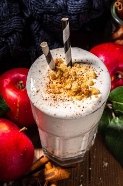 Ev yapımı elmalı turta milkshake, tart parçacıkları ve baharatlı kırmızı sonbahar elma proteini smoothie, sıcacık ahşap arka planda mevsimlik sağlıklı bir kahvaltı içeceği.