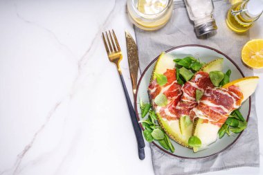 Prosciutto hamon ve yeşil yapraklı taze kavun salatası karışımı, sonbahar meyve sebze salatası, tabakta porsiyon, beyaz mermer arka plan fotokopi alanı.