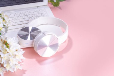 Bahar ofisi işyeri, blog düz zemin. Beyaz dizüstü bilgisayar, kulaklık, tablet, pembe inci arka planda bahar çiçekleri, dizüstü bilgisayarda yazı yazan bir kız..