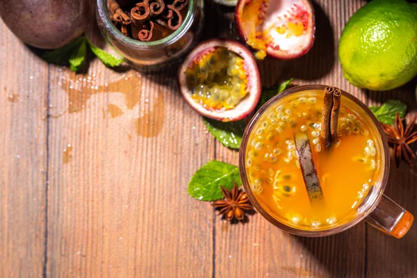 Passion fruit hot tea drink with fruity juice, cinnamon, lime, over wooden background with fresh passion fruit and spices