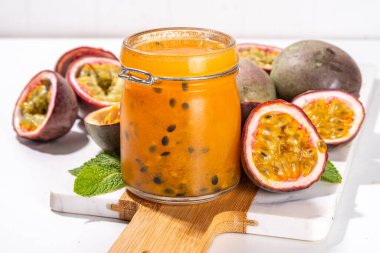 Küçük kavanozda ev yapımı tutku meyvesi reçeli, beyaz mutfak arka planında taze tutku meyvesi ve nane yaprakları kopyalama alanı.