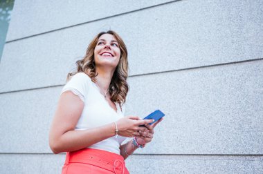 Yazlık giysiler giymiş, akıllı telefon kullanan ve şehirde dikilen kadınların yan görüntüsü..