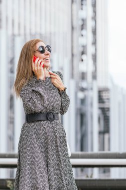 Sonbahar elbiseli bir kadın akıllı telefon kullanıyor ve şehirde dikiliyor..