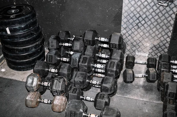 一堆堆厚重的黑色哑铃躺在靠近墙壁的体育馆地板上 — 图库照片