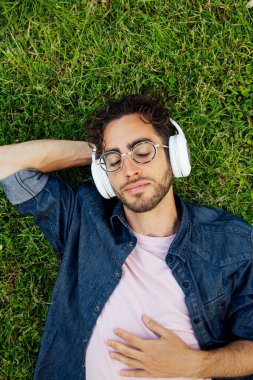Bahçede kulaklıklarla yatan yakışıklı genç bir hippi portresi..