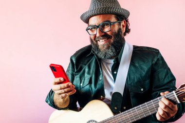 Akustik gitarlı akıllı telefon kullanan mutlu sakallı adam..