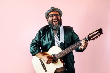 Mutlu sakallı adam pembe arka planda akustik gitar çalıyor..