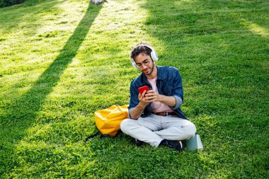 Kulaklık ve cep telefonuyla müzik dinleyen yakışıklı genç hippi portresi..
