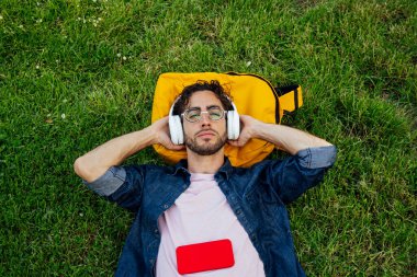 Kulaklık ve cep telefonuyla müzik dinleyen yakışıklı genç hippi portresi..